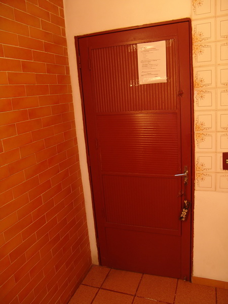 A porta do quarto, de metal, com vidros pintados, tosco